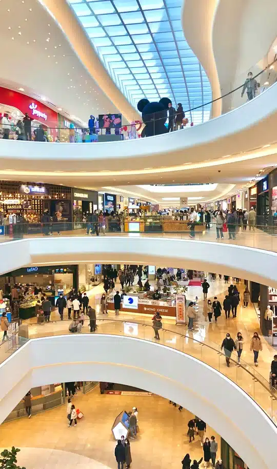 Busy multi-level shopping mall with curved balconies under a glass skylight