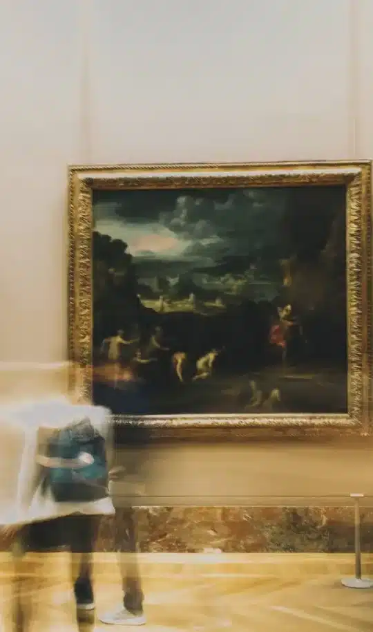 Museum gallery with framed paintings on the wall and visitors walking past