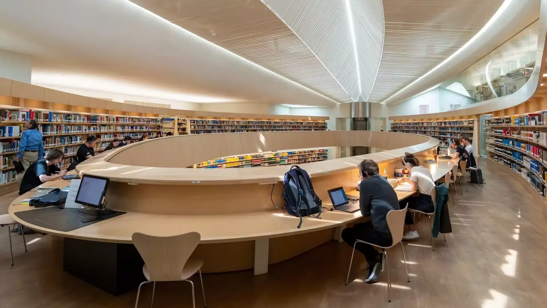 Library reading room with curved bookshelves and people working at a long desk